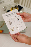 That Grazing Table Signature Wine Charm Set with six travel-inspired charms including compass, airplane, postcard, and olive branch on a branded keepsake card