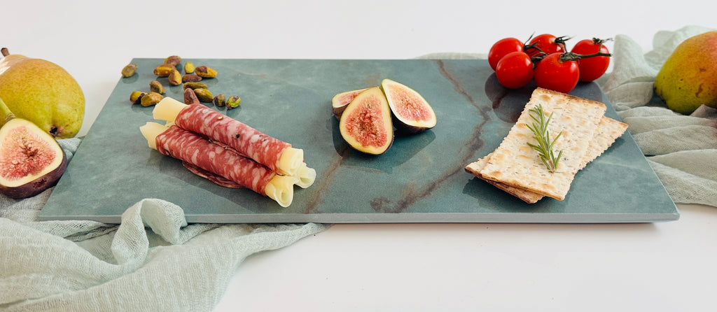 Sevilla olive green porcelain charcuterie board with amber veining, lightly styled with salami-wrapped cheese, figs, pistachios, crackers and cherry tomatoes